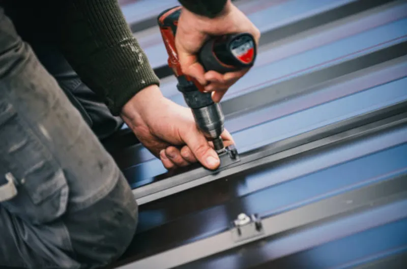 Worker using a power drill to fasten metal roofing panels.